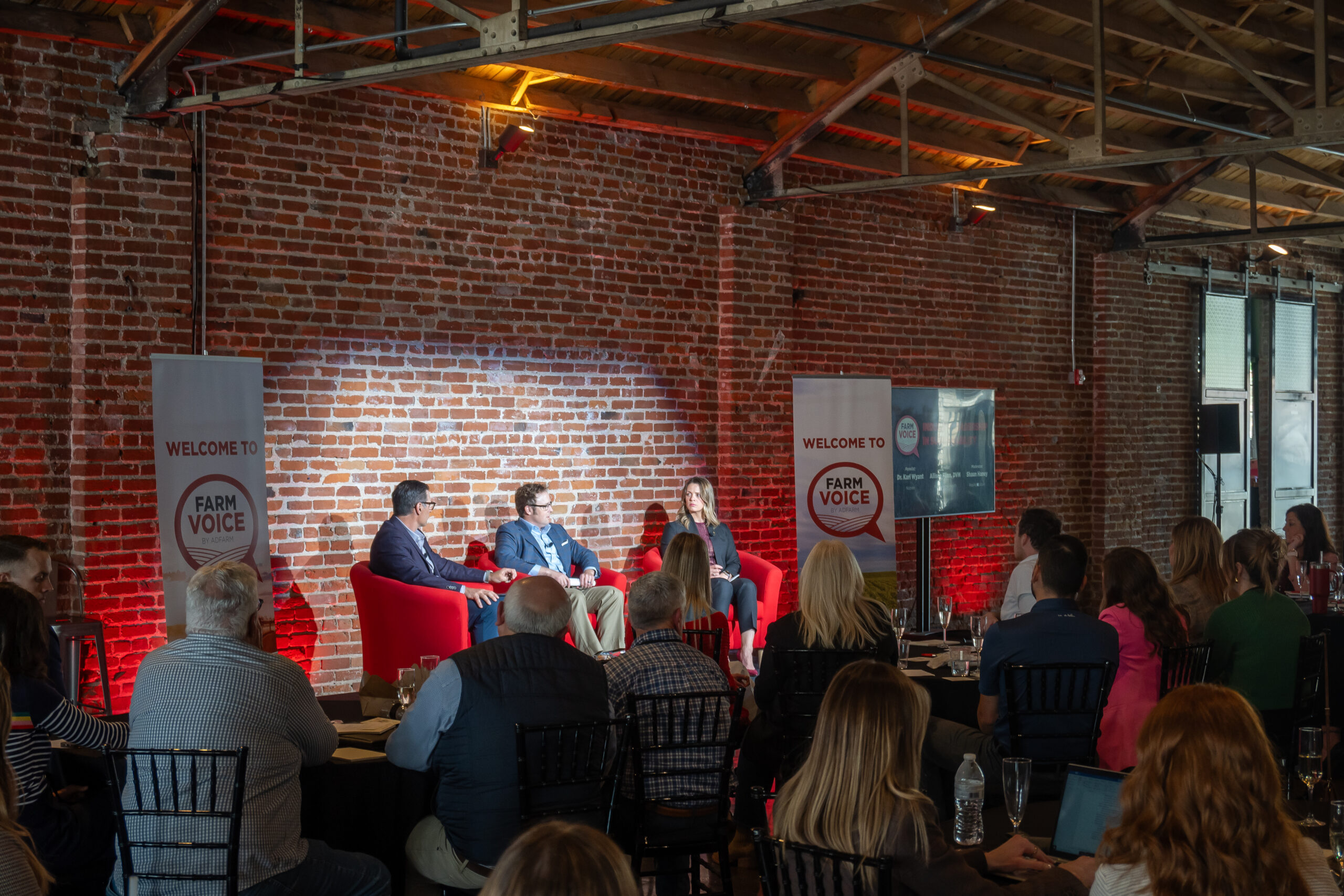 Sustainability Industry Leadership Panel at conference featuring two men and one woman, framed by farm voice banners and conference attendees watching